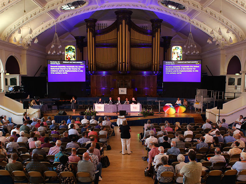 Assembly meeting with someone speaking to the panel