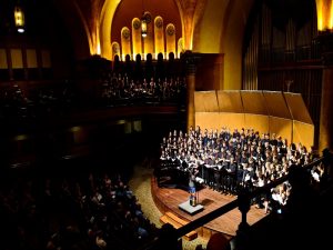 Large choir performing on stage with a conductor