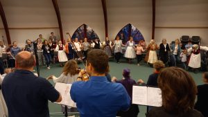 A group of people watching Hungarian muscians play music and dancers in traditional costumes dance.