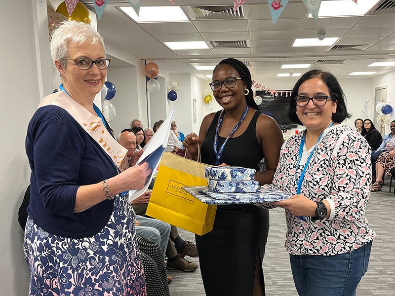 Three friends, two of who are giving presents to the third person.